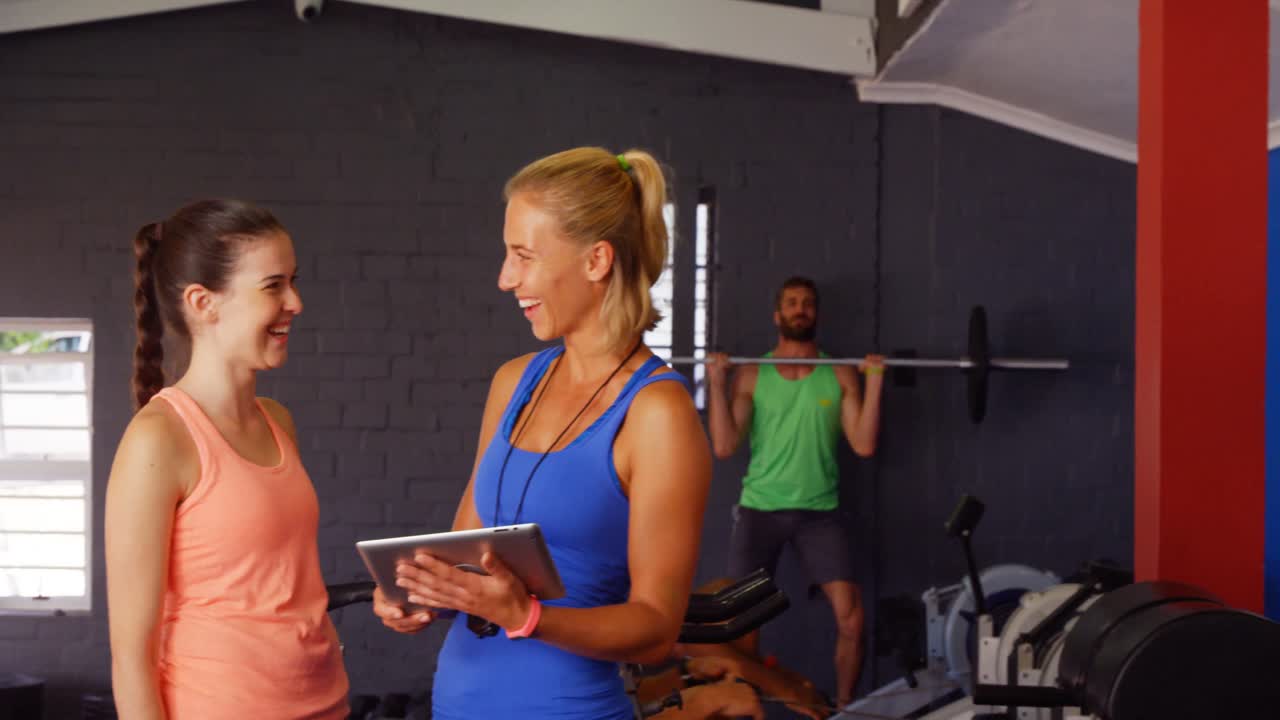 디지털 태블릿을 사용하는 동안 여성 트레이너가 여성과 상호 작용합니다.