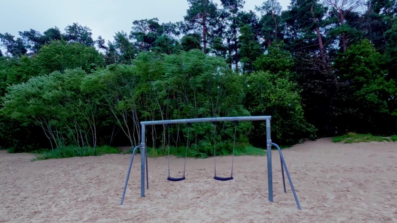 Altalene abbandonate sulle dune di sabbia sullo sfondo di una rigogliosa pineta sulla costa baltica durante una giornata ventosa e nuvolosa, riprese con un'inquadratura fissa d'ambiente