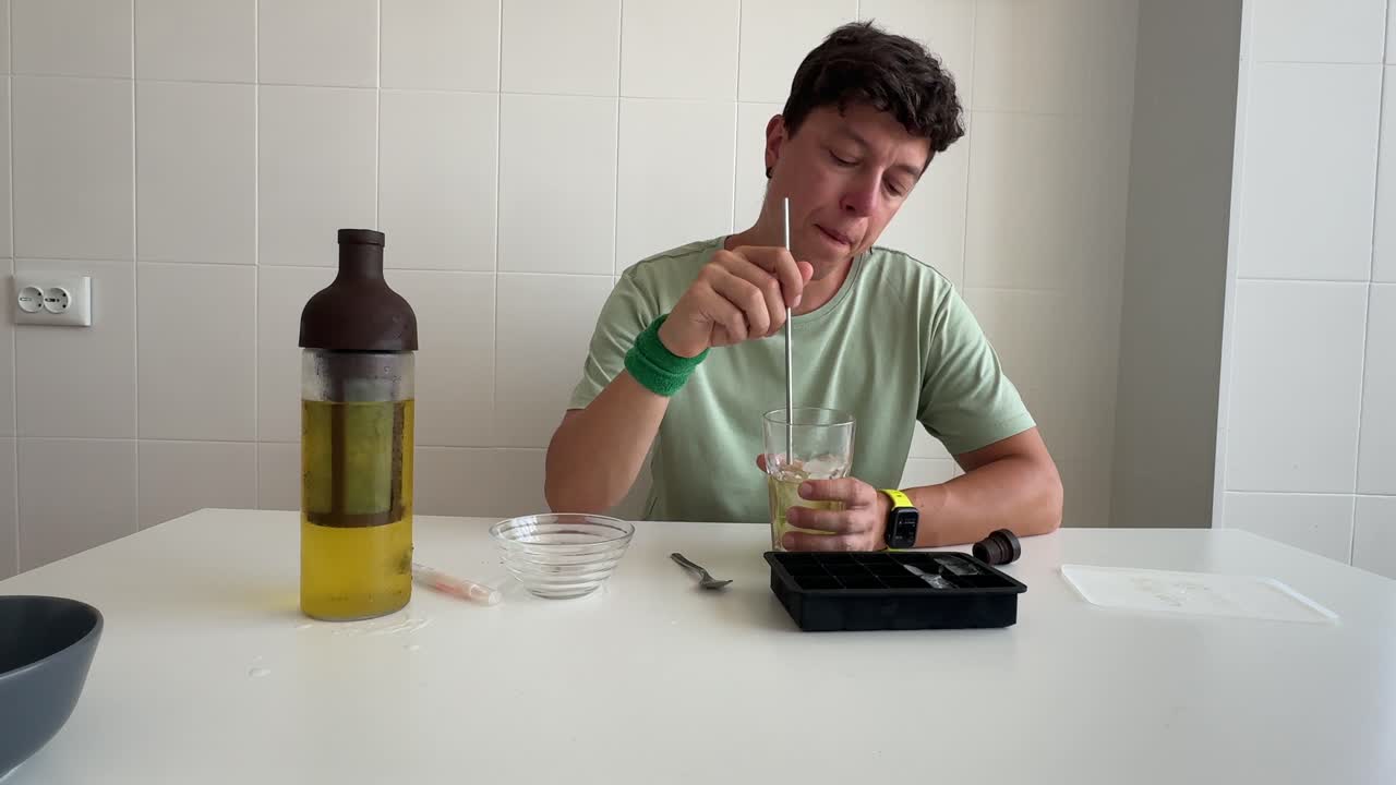 Giovane uomo che mescola e sorseggia una bevanda fredda in cucina.