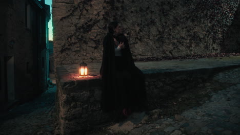 cold woman with cloak and lantern sitting at night in the medieval city