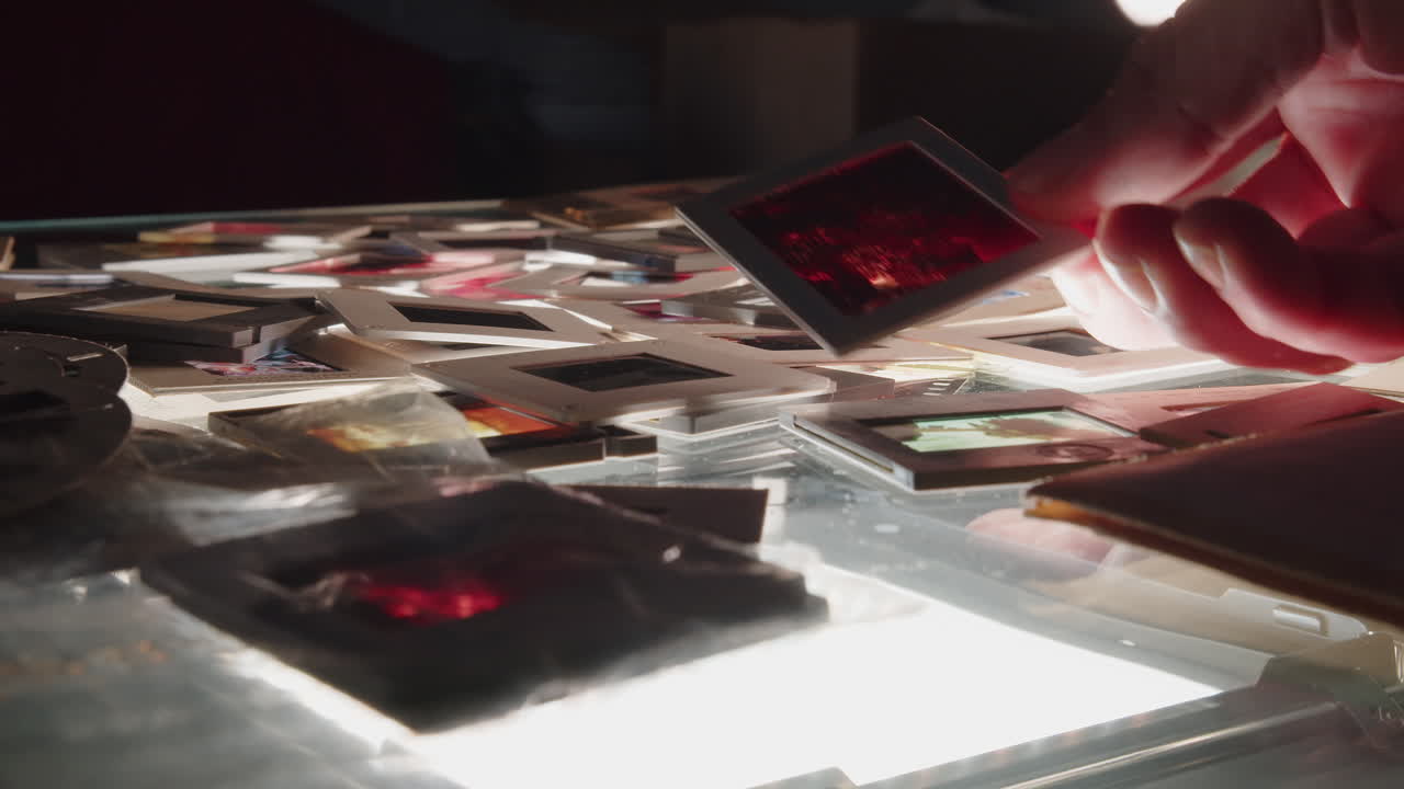 Photographer's hands sort through a pile of colour slides on a backlit table