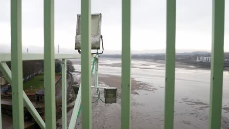 Industrial-security-railings-bars-fence-barrier-closeup-overlooking-low-tide-waterfront-from-high-bridge-view-dolly-slow-left