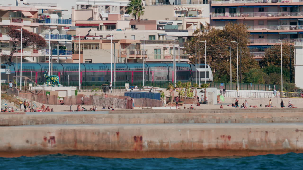 Cannes, France - October 6, 2025: A modern train passes along the coastline near the beach, while people walk and relax nearby