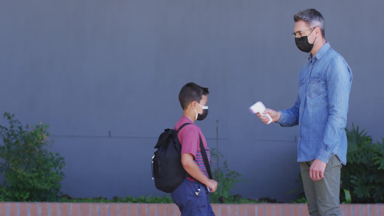 다양한 남성 선생님이 학교 소년의 온도를 측정하고, 모두 얼굴 마스크를 착용하고 있습니다.