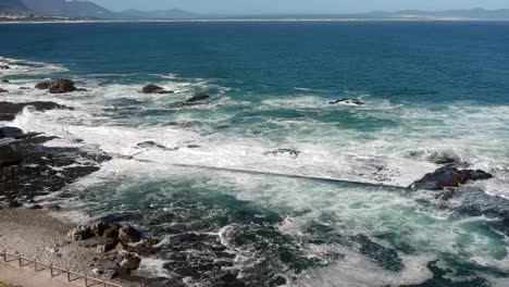 Angled-drone-view-of-tidal-pool-and-rocky-coastline,-with-waves-crashing