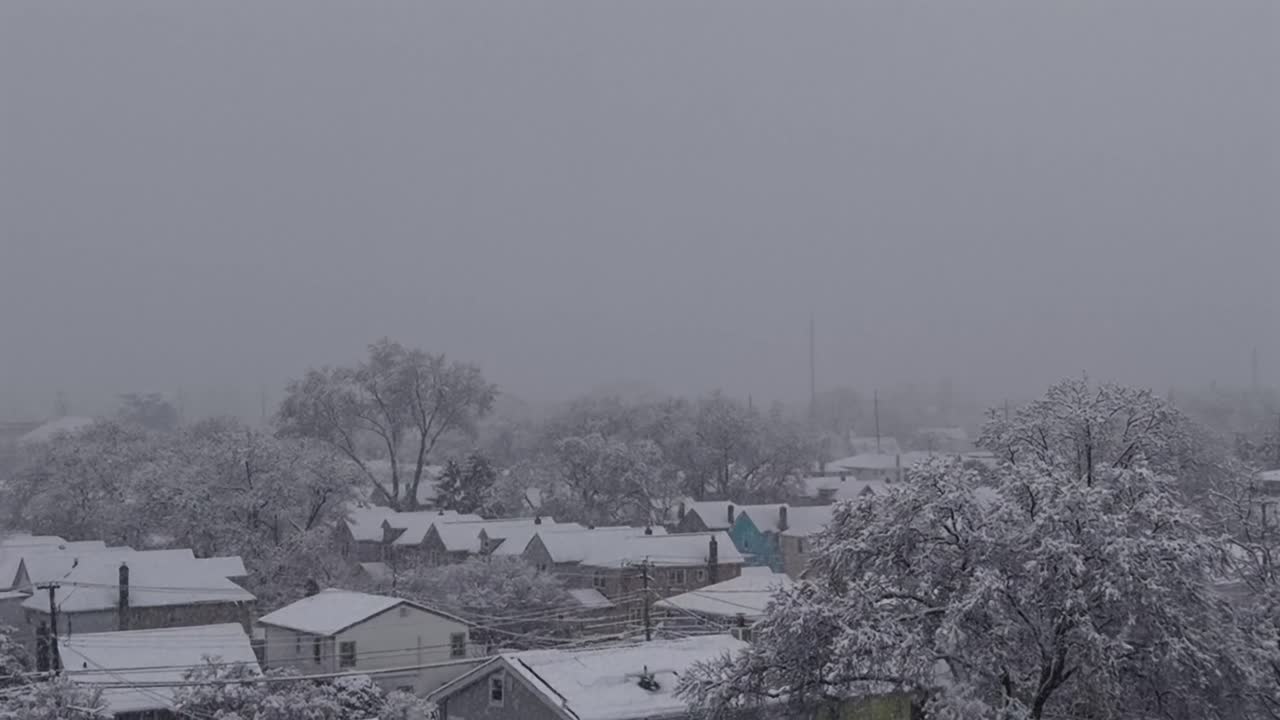 An aerial view of the suburban neighborhood of Valley Stream on Long Island, NY. Taken on a winter morning. The camera dolly in, boom up over the residential area with snow falling and on the ground