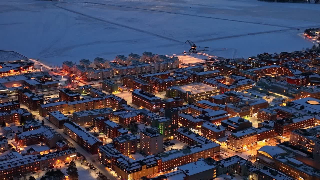 el crepúsculo desciende sobre el paisaje urbano cubierto de nieve de luleå, luces callejeras brillantes, vista aérea