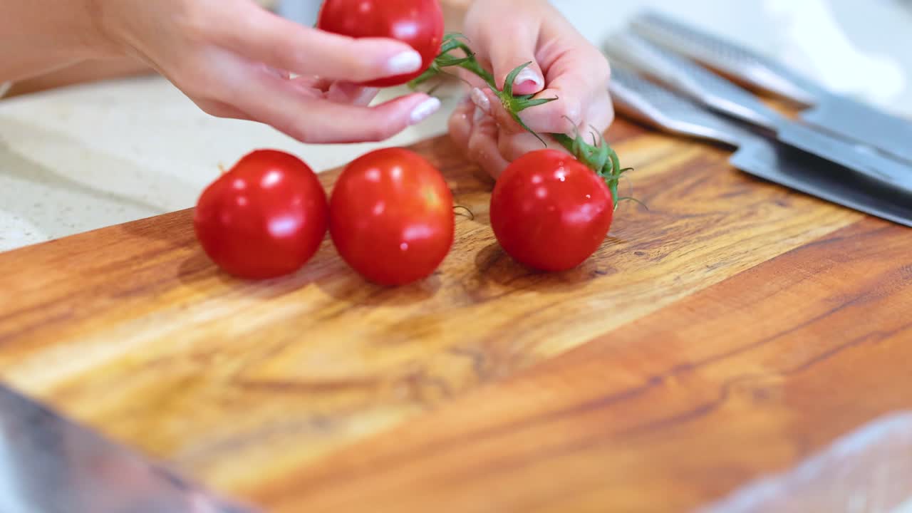 Hands organize fresh tomatoes on a wooden cutting board under bright lighting, showcasing a kitchen setting
