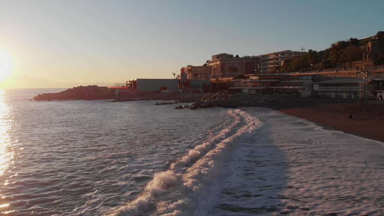 aerial: olas que golpean la arena al atardecer en corso italia, genova, con llamaradas ópticas