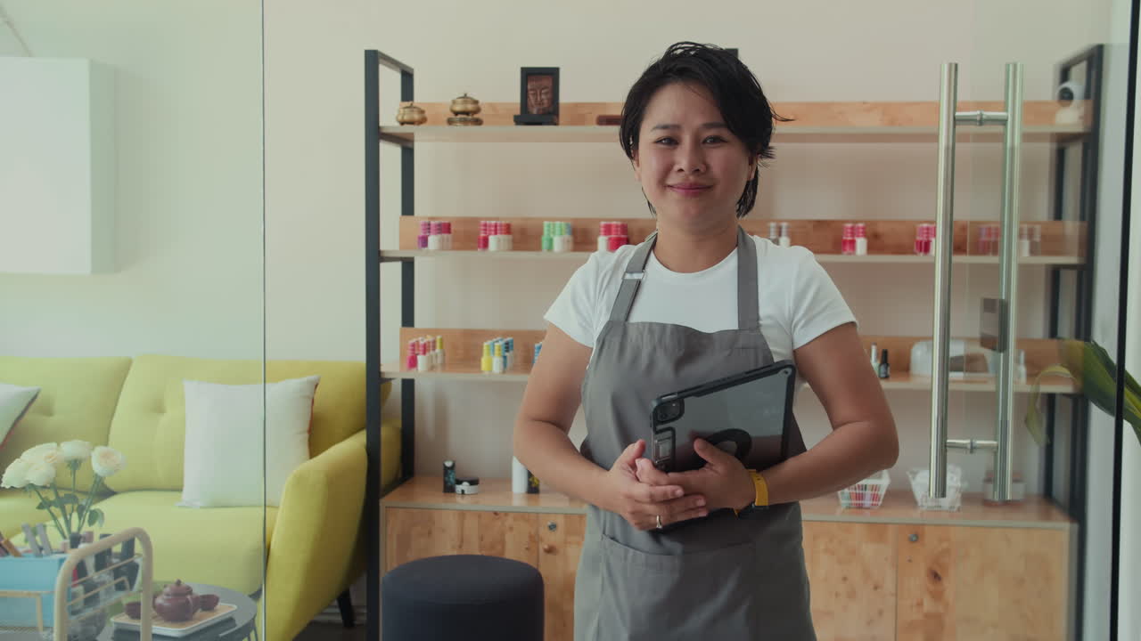 Retrato de una manicurista asiática con una tablet en un salón de manicura