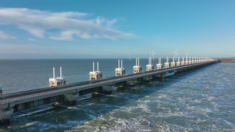 aerial slow motion shot of an open eastern scheldt storm surge barrier and wind turbines in zeeland, the netherlands on a beautiful sunny day with a blue sky