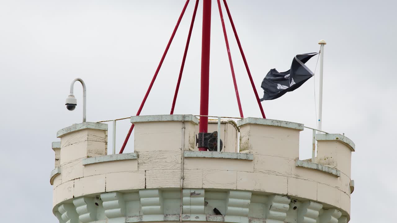 Black flag waves atop round castle tower under overcast daylight, captured in steady telephoto shot