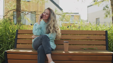 woman sitting on bench in park and talking on phone