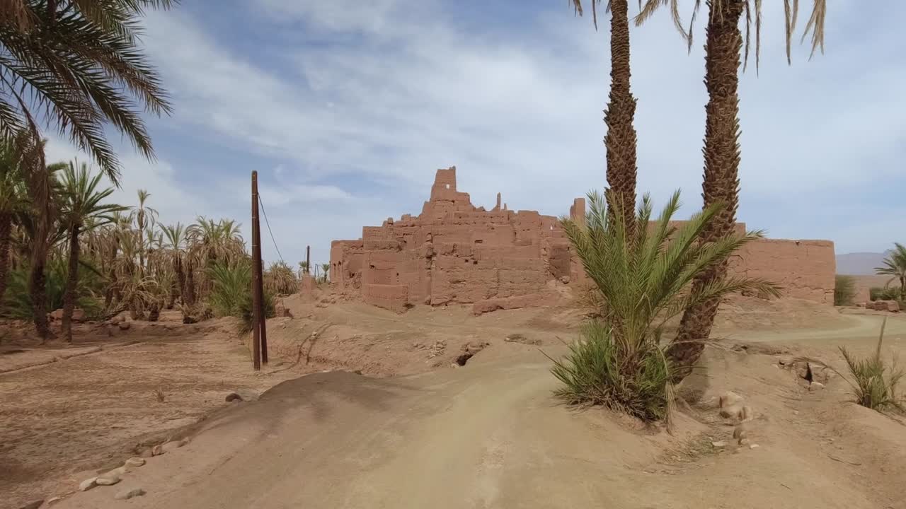 Point of view of a driver crossing an oasis and arriving to an abandoned kasbah