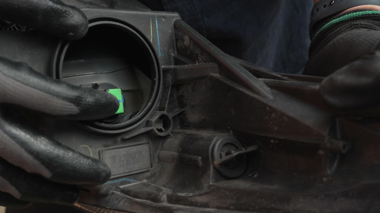 Automotive mechanic wearing gloves unplugging the electrical connector on the back of a car headlight