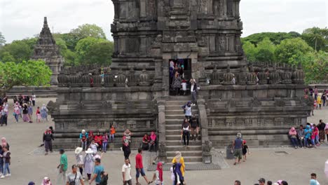 indonesia,prambanantemple on a cloudy day,camera tilts up slowly from ground level to the top,some people walking down the stairs and some others climbing the stairs of the temple.trees behind and sky