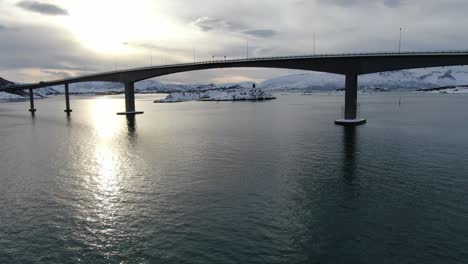 drone view in tromso area in winter flying next to a bridge connecting two islands full of snow over the sea in norway