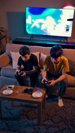two boys playing video games in a living room at night
