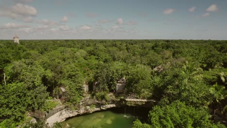 zoom-out-tilt-up-footage-of-natural-cenote-with-eco-hotel-in-Mexico-in-sunny-day