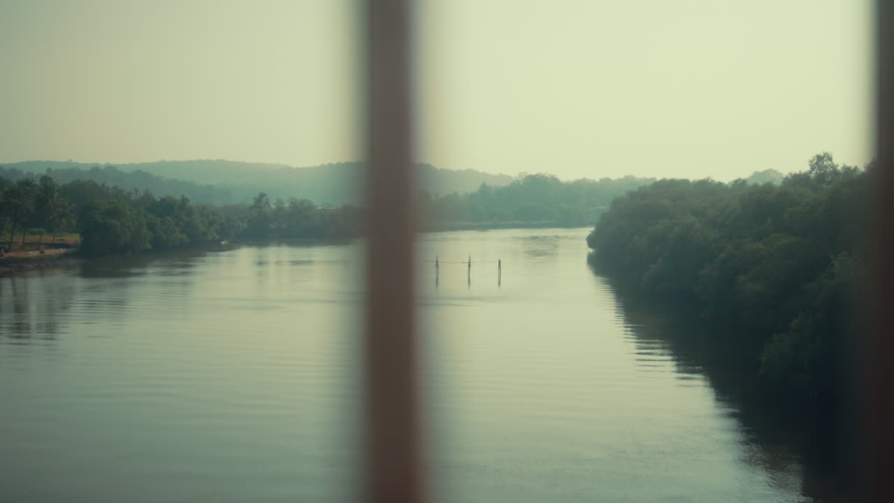 Pan left shot revealing a wide river landscape with calm water, distant trees and soft natural light