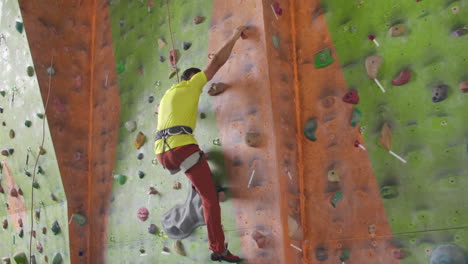 climber moves on the mountain in a room with a rope on the insurance and a bag for chalk overcoming the height rises to the top in slow motion