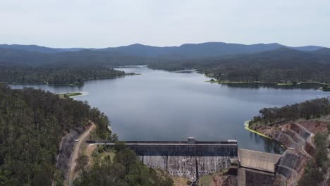 Vista-Aérea-De-Una-Presa-Y-Un-Muro-De-Presa-Con-Montañas-Al-Fondo