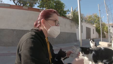 Sad-brunette-lady-wearing-a-mask-feeding-cats-in-a-deserted-village