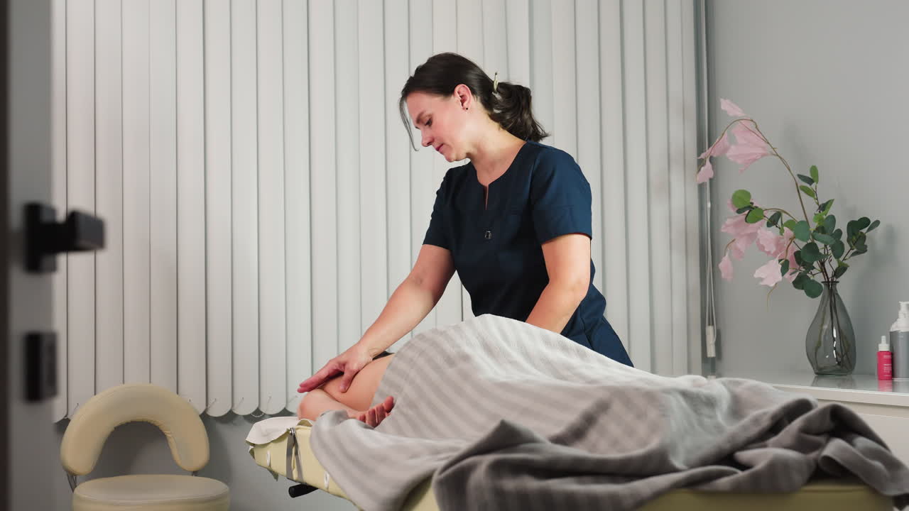 Massage therapist massaging shoulders of model on massage bed in spa room with flower vase and massage cream on shelf under soft ambient lighting creating serene wellness experience
