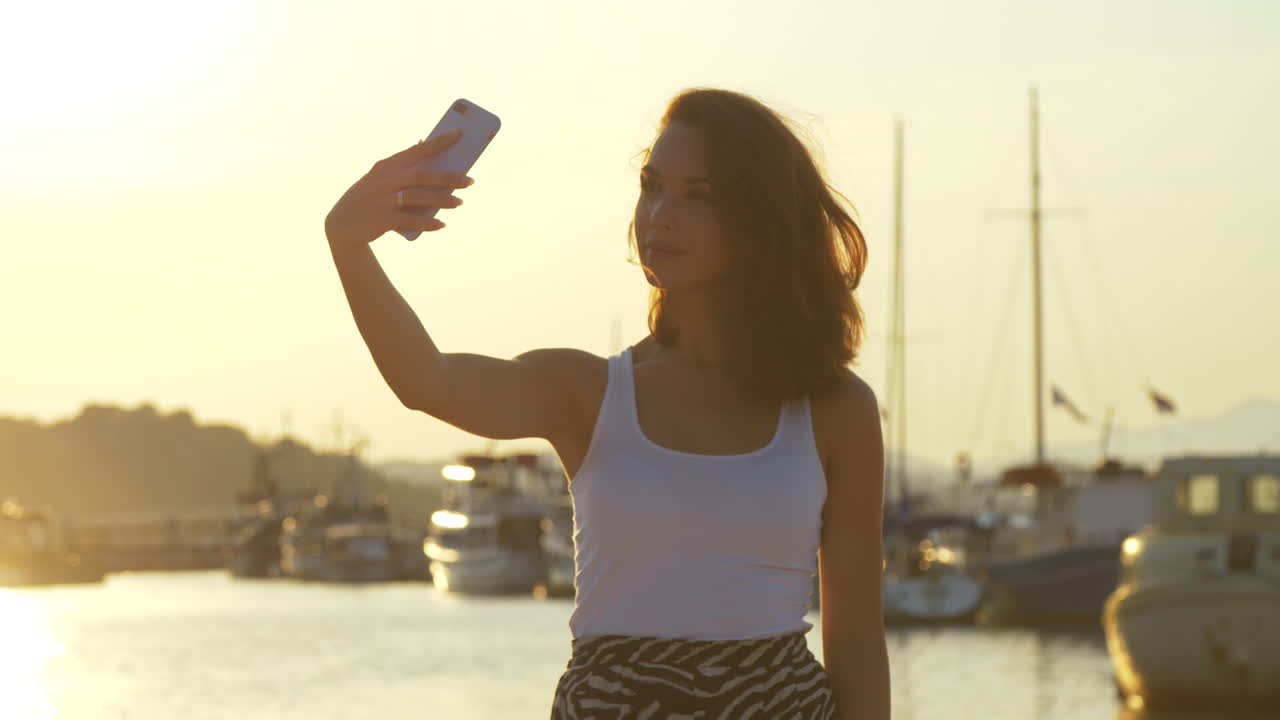 mujer feliz tomando una foto móvil en el puerto de la noche. chica de viaje posando para una selfie
