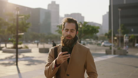 portrait-of-attractive-stylish-young-bearded-hipster-man-texting-browsing-using-smartphone-messaging-app-in-city