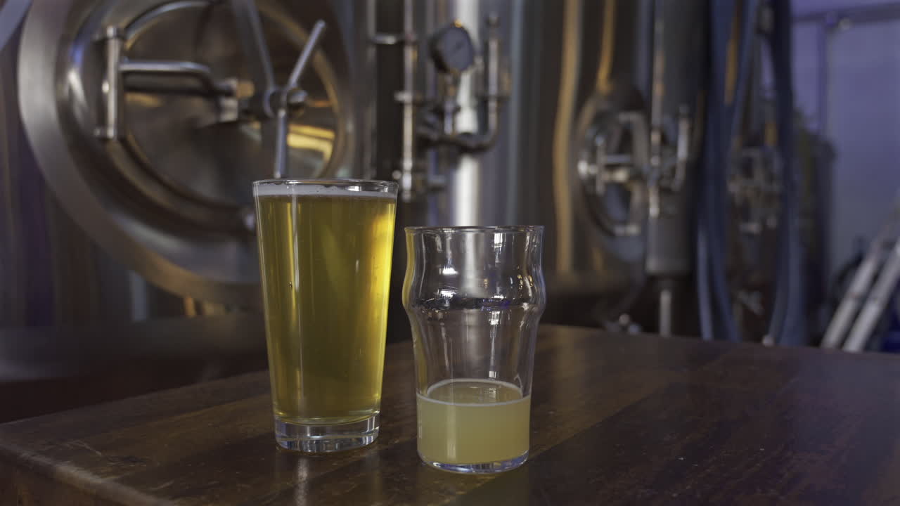 Close up of two beer glasses with stainless steel tanks on the background