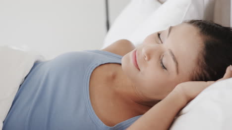 Portrait-of-happy-biracial-woman-lying-in-bed-at-home,-slow-motion