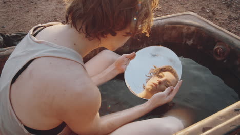 woman looking in mirror and washing face in dirty bath