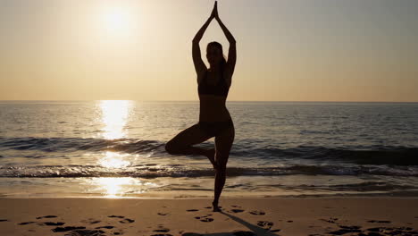 woman practicing yoga on the beach at sunrise
