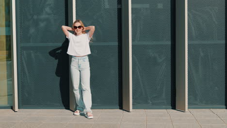 mujer con una camiseta blanca y vaqueros azules ligeros frente a un edificio moderno