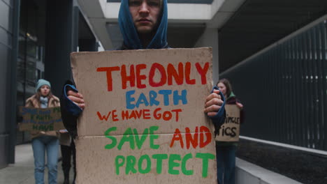 close up view of young male activist holding a cardboard placard during a climate change protest while looking at camera