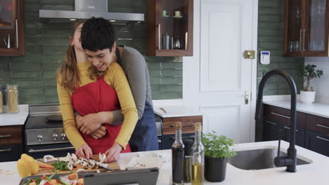 Feliz-Pareja-De-Lesbianas-Caucásicas-Preparando-Comida,-Abrazando-Y-Usando-Tableta-En-La-Cocina,-Copiando-Espacio