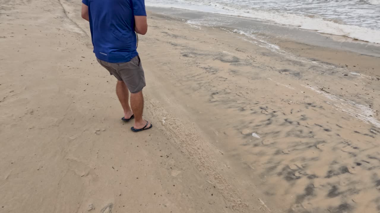 un fotógrafo lucha por mantener el equilibrio en una playa ventosa, capturando la interacción dinámica con la naturaleza