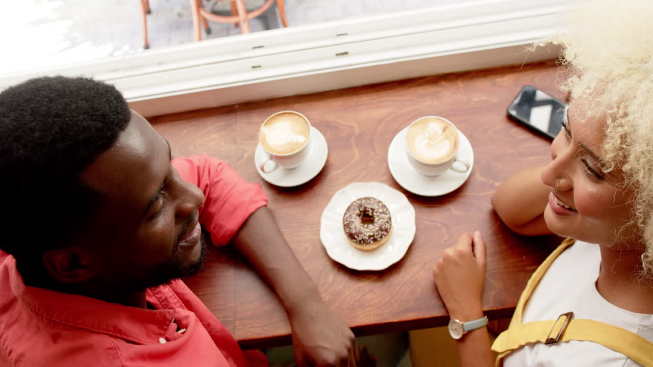 A happy couple of a young African American man and a young biracial woman enjoy coffee together
