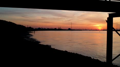 disparo de dron inclinado hacia abajo que revela la silueta de una niña parada en un puente con un paisaje nublado de puesta de sol de hora dorada en el fondo