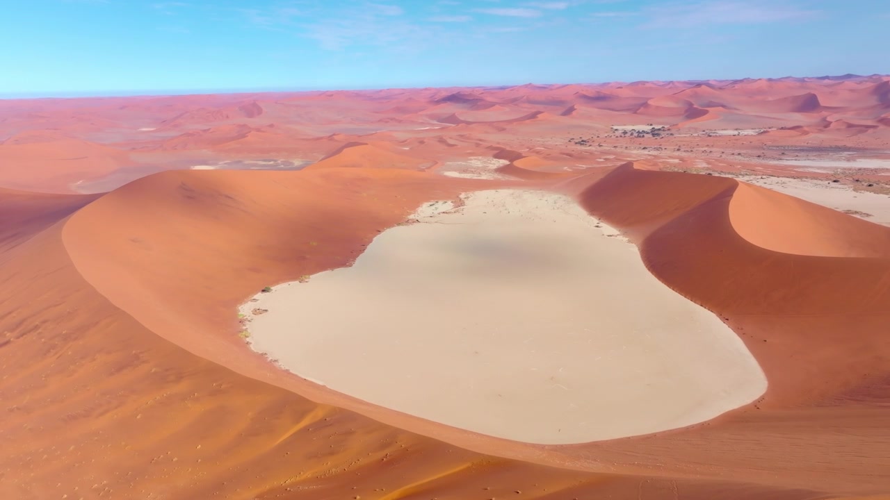 Vista aérea de dunas de areia vermelha curvando-se em torno da bacia branca brilhante de Sossusvlei no deserto do Namibe. As imponentes dunas vermelhas brilham contra as bacias de argila pálidas e rachadas desta antiga paisagem desértica selvagem.