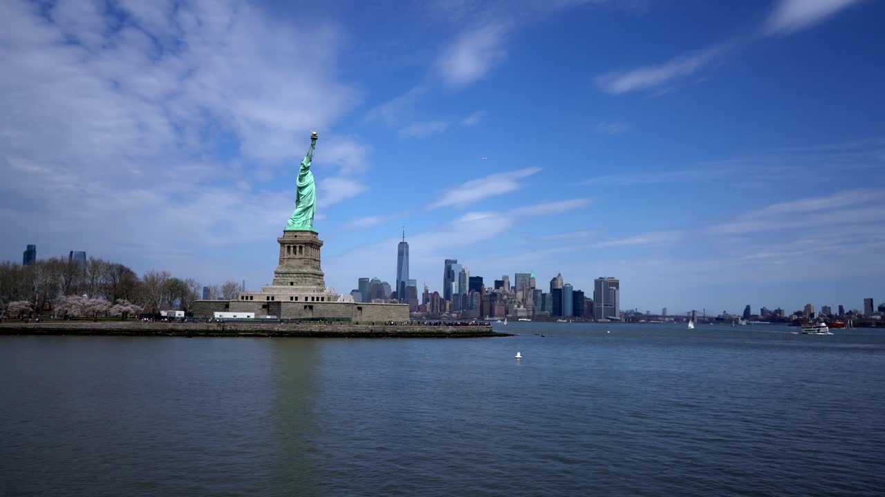 Isola della Statua della Libertà con lo skyline di New York sullo sfondo attraverso l'acqua, ampia.