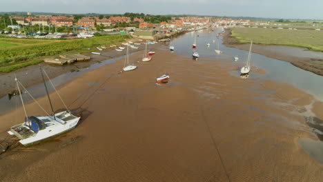 low establishing drone shot at low tide down wells-next-the-sea creek with small sailing boats and dinghies with salt marsh and harbour north norfolk uk east coast