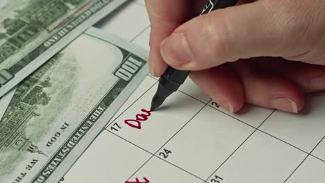 female hand marking the day in calendar by writing day debt as a reminder using a red marker.