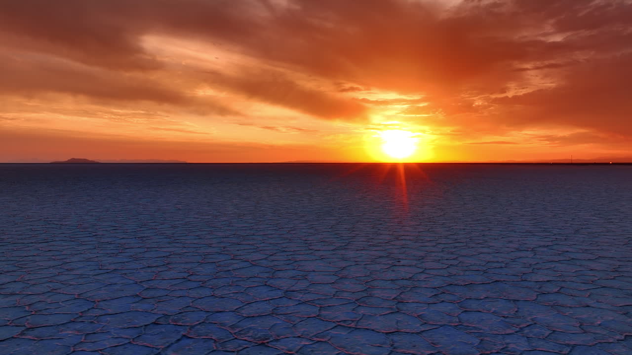 El sol se pone en el horizonte en Bonneville Salt Flat, Utah, Estados Unidos. El cielo nuboso se tiñe de naranja y el paisaje se ve azul. Vista aérea.