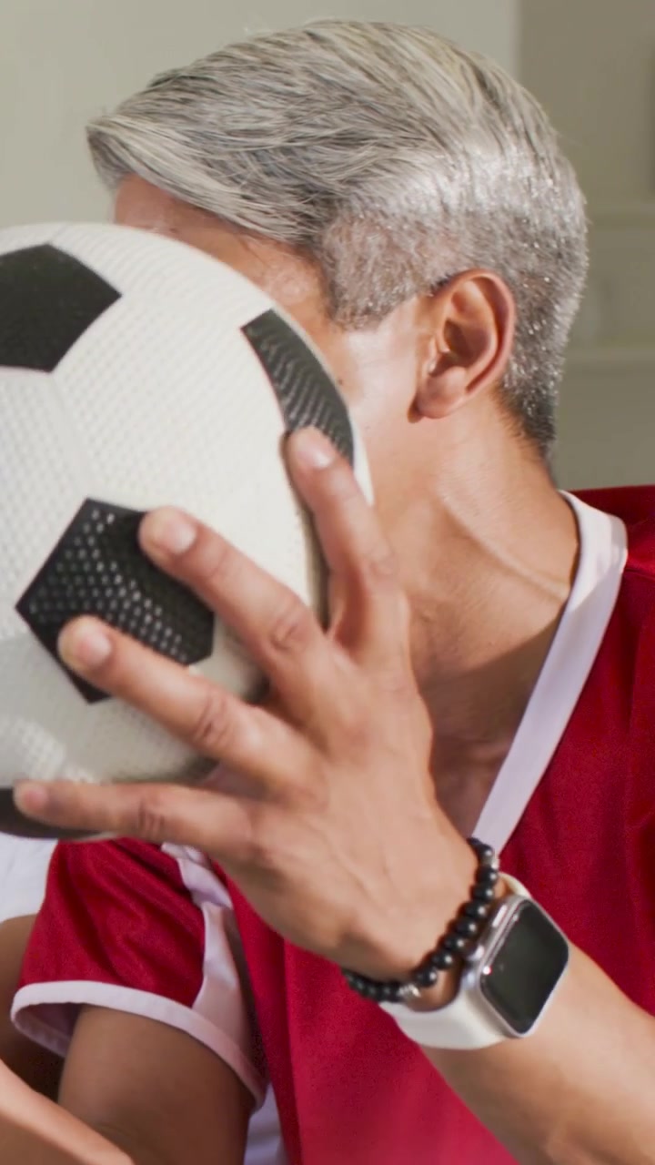 Video verticale: Uomo in maglia rossa che reagisce a un rumore fuori campo, portando l'altoparlante alla bocca, a casa.