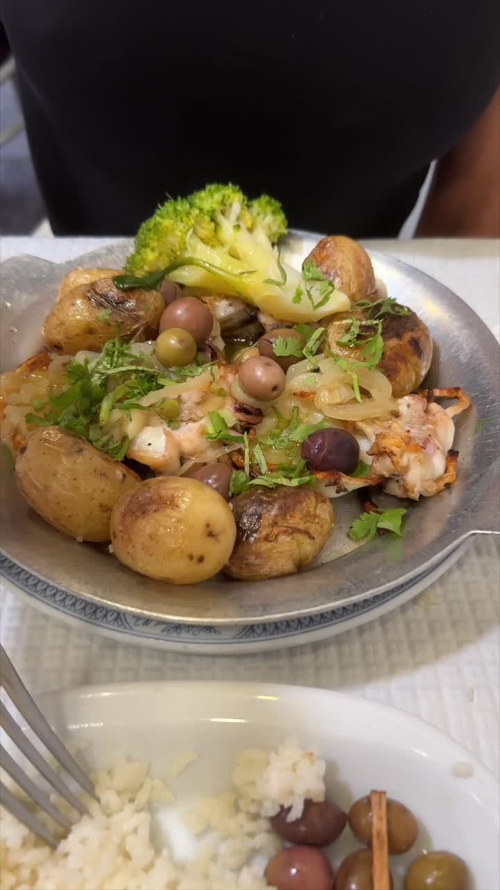 A delicious seafood meal with roasted potatoes, broccoli, and olives, served with rice, fries, and lemon