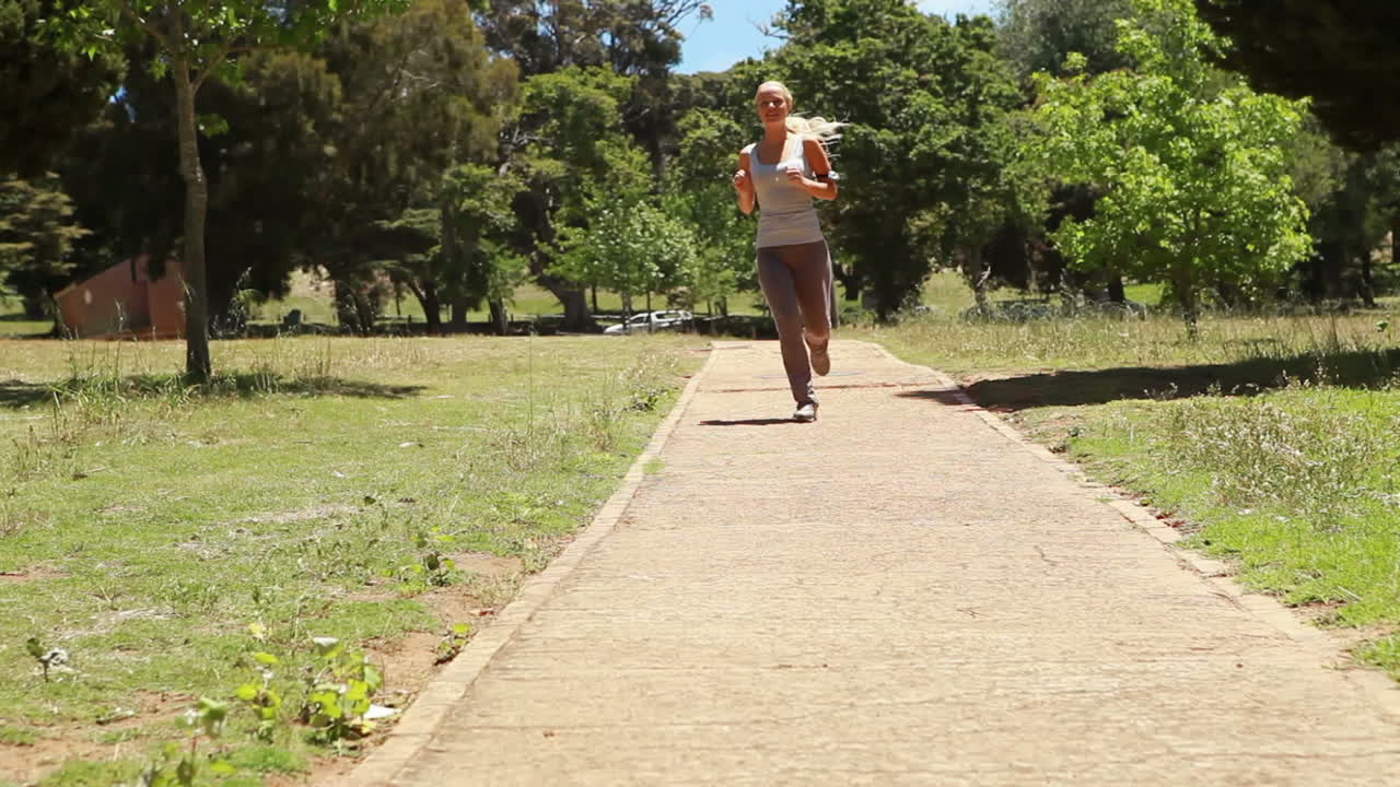 Uma mulher trota por um caminho em direção e passando pela câmera