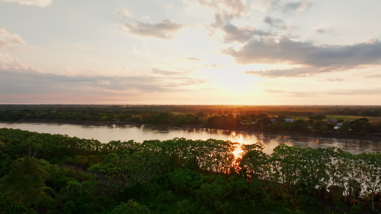 Drone footage over San José del Guaviare, Colombia, capturing dense rainforest canopy, riverbanks, and a crossing point within the remote jungle scenery