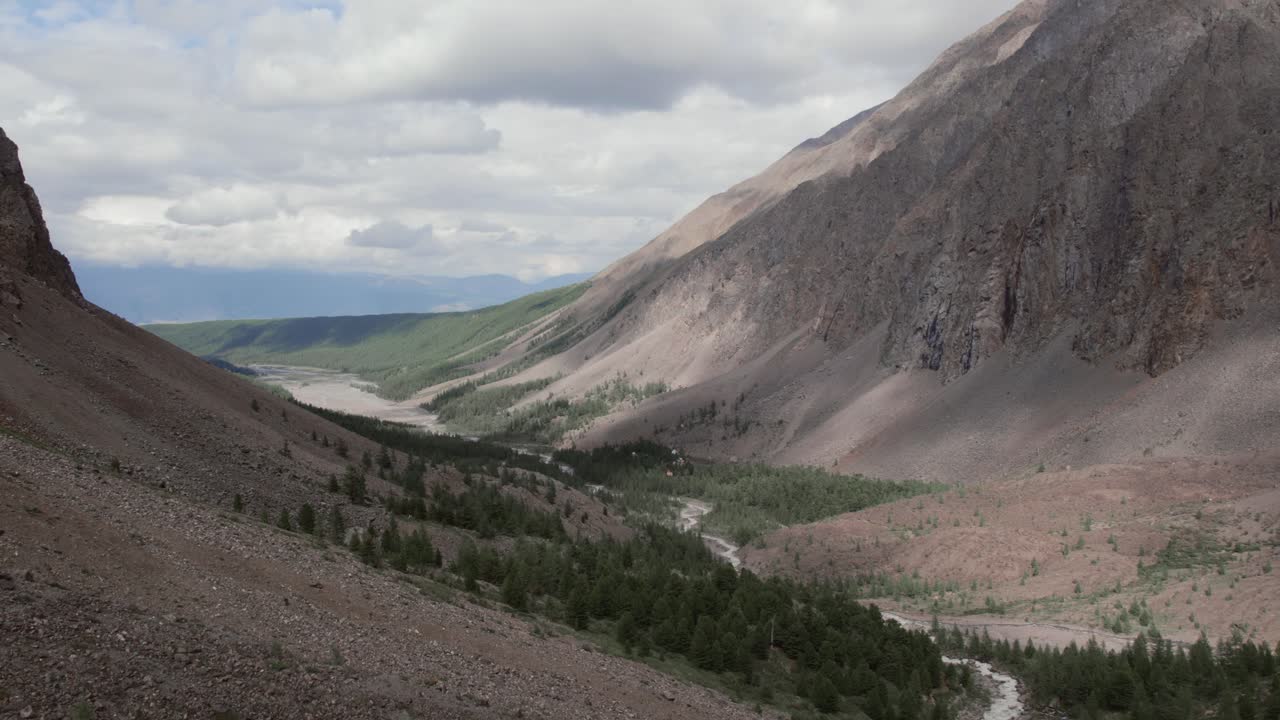 Ampio paesaggio montano della Valle dell'Aktru con pendii rocciosi, fiume e foresta di conifere sotto un cielo nuvoloso, Repubblica dell'Altai, Russia, una vista panoramica di viaggio nella natura selvaggia.